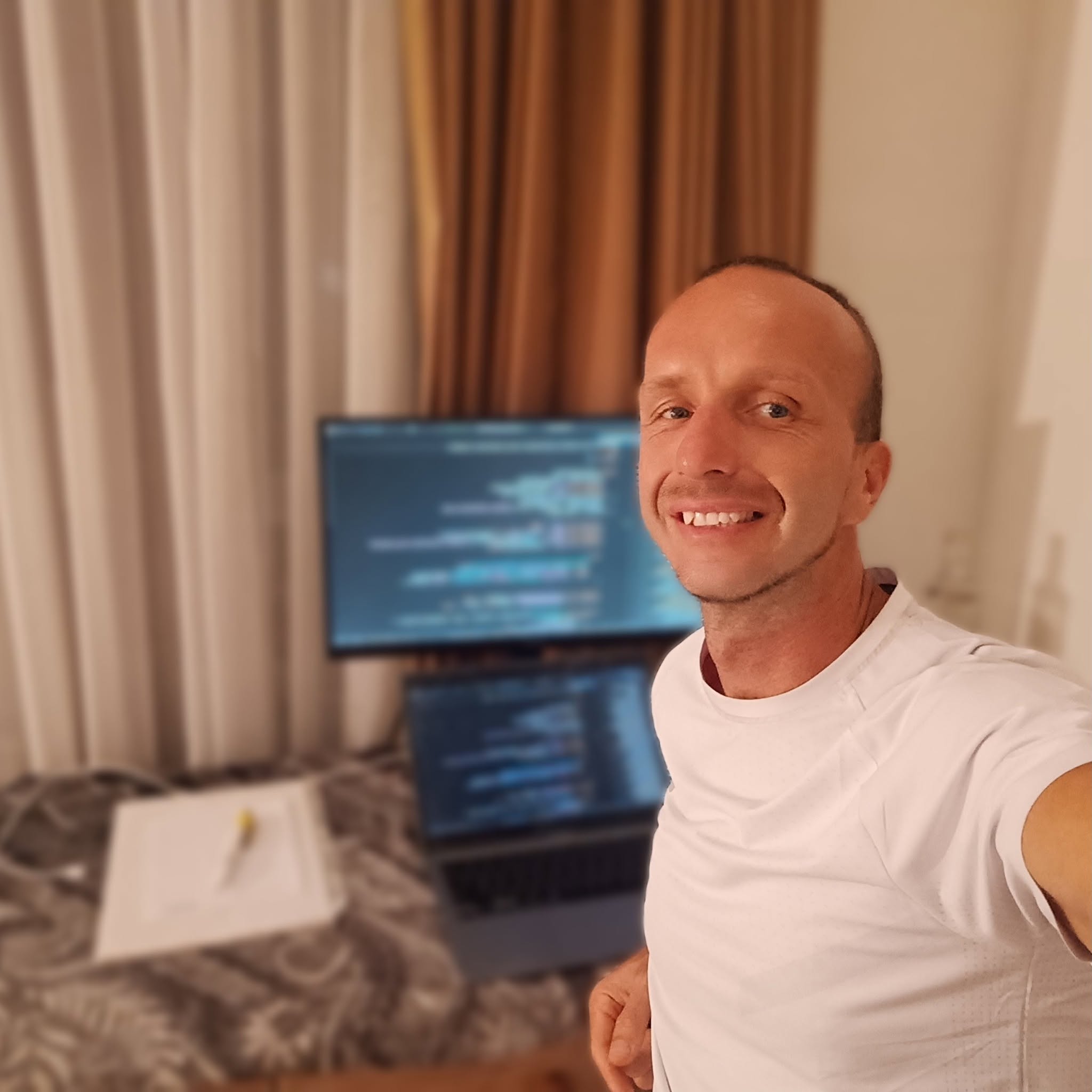 René Doháň smiling beside a laptop and monitor displaying source code.