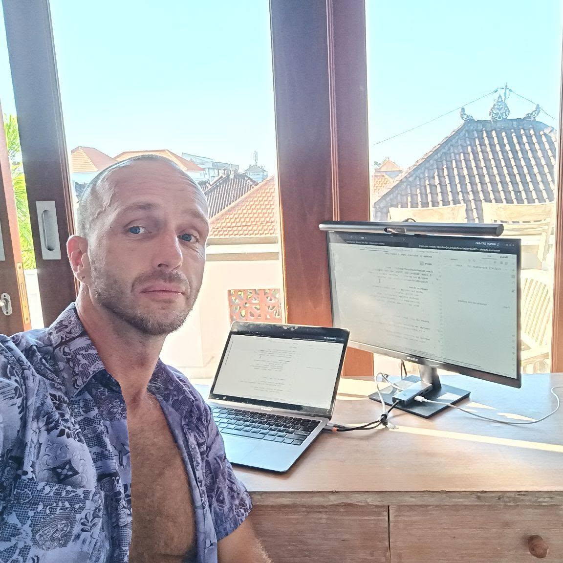 René Doháň seated at his desk with a laptop and external monitor.